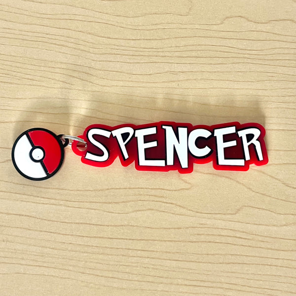 Keychain with 'SPENCER' text and Pokémon logo on a wooden surface