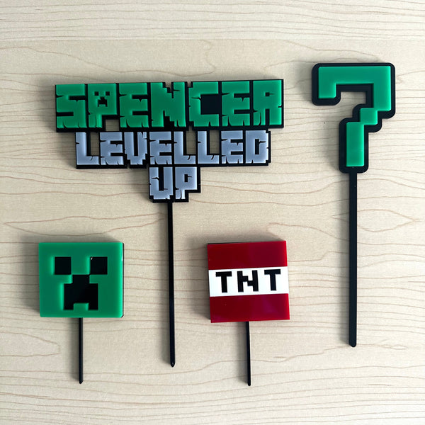 Decorative topper with 'Spencer Levelled Up' text, Creeper head, TNT block, and question mark symbol on a wooden background.