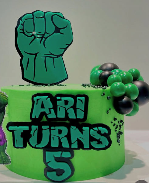 Green cake with a raised fist decoration and 'ARI TURNS 5' text on a plain background