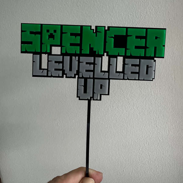Decorative cake topper with 'Spencer Levelled Up' text on a white background