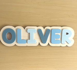 Wooden name block with 'OLIVER' in blue letters on a wooden background