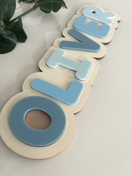 Wooden name puzzle with blue and beige letters spelling 'Oliver' on a light background.