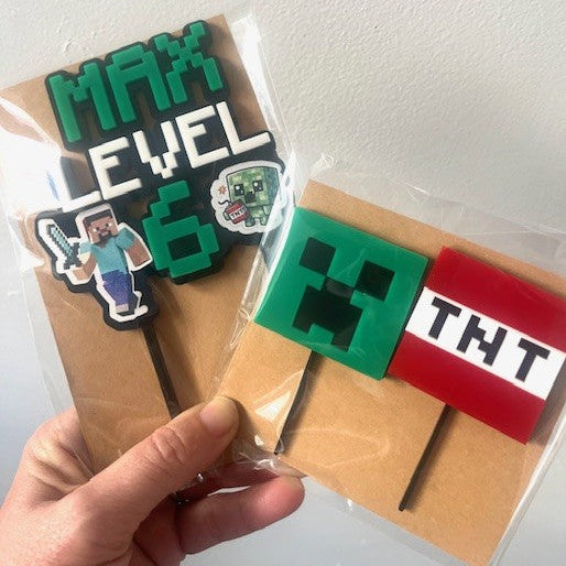 Two Minecraft-themed bookmarks with 'MAX LEVEL' and 'TNT' designs held by a hand against a white background.