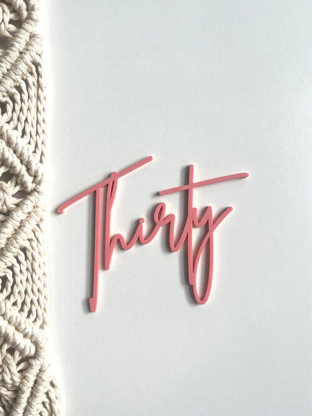 Pink 'Thirty' decoration on a white background with macrame wall art.