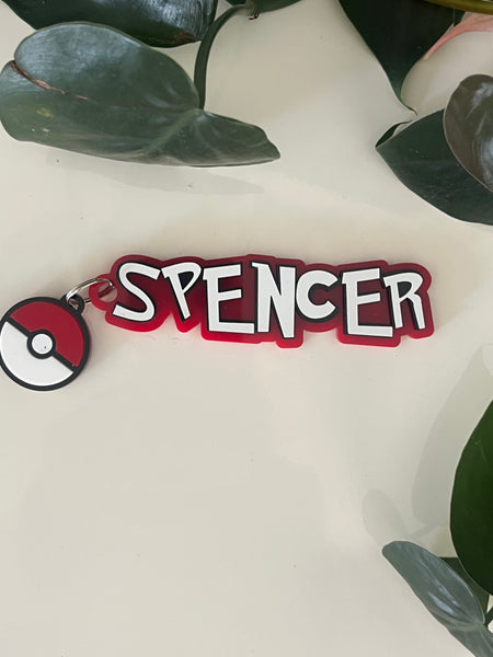 Red and white 'SPENCER' keychain with a Pokémon logo on a light background