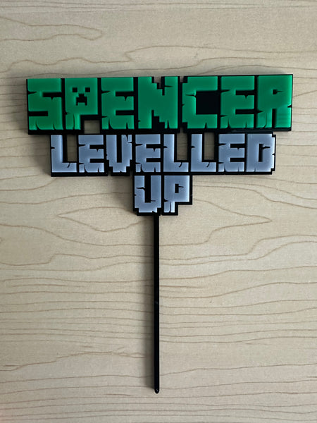 Decorative topper with 'SPENCER LEVELLED UP' text on a wooden surface