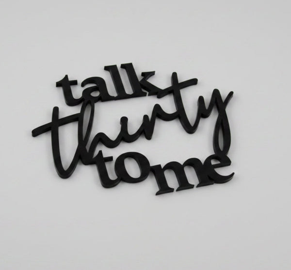 Black cake topper with 'talk thirty to me' text on a white background