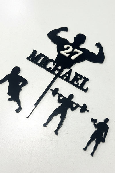 Personalized fitness cake topper with black silhouette cutouts of athletes, the name MICHAEL, the number 27, and a muscular figure silhouette on a white background.