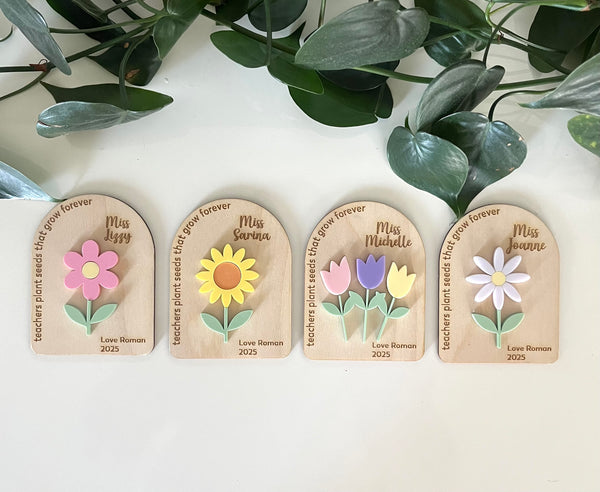 Four personalised wooden plaques with floral designs and engraved names on a white surface with green leaves in the background.